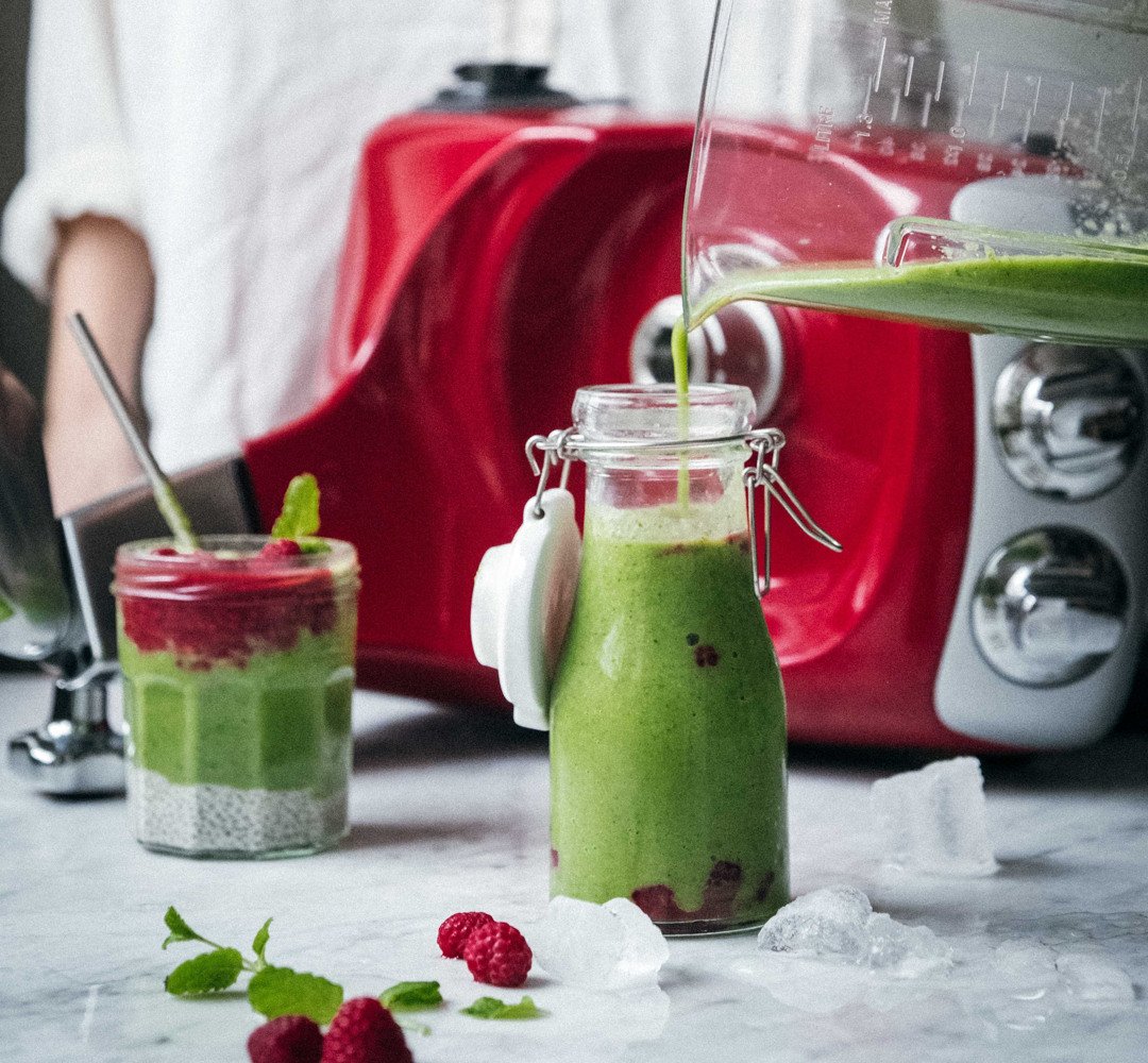 A woman pouring a green smoothie into a glass jar