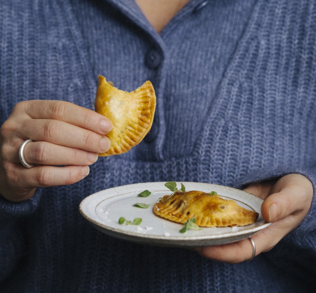 En kvinna som håller en tallrik med empanadas i sina händer.