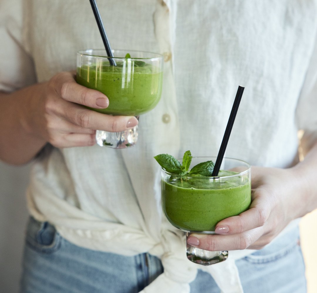 A person holding two glasses of green smoothie.