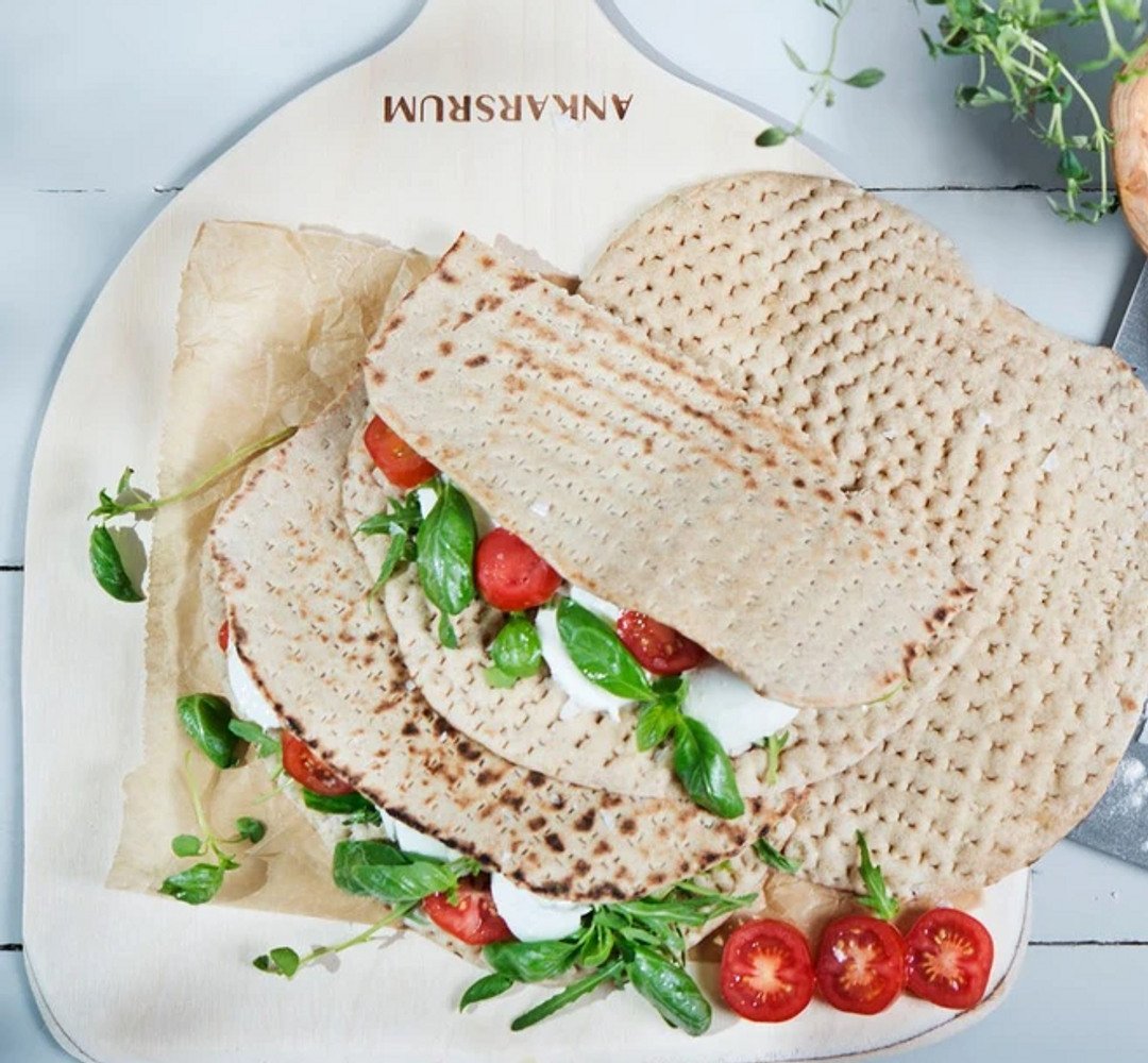 Flatbread rolls on a wooden board, filled with basil, mozzarella, and tomato.
