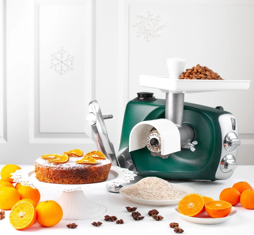 Ankarsrum Assistent grating almonds. A cake topped with orange slices stands beside it.