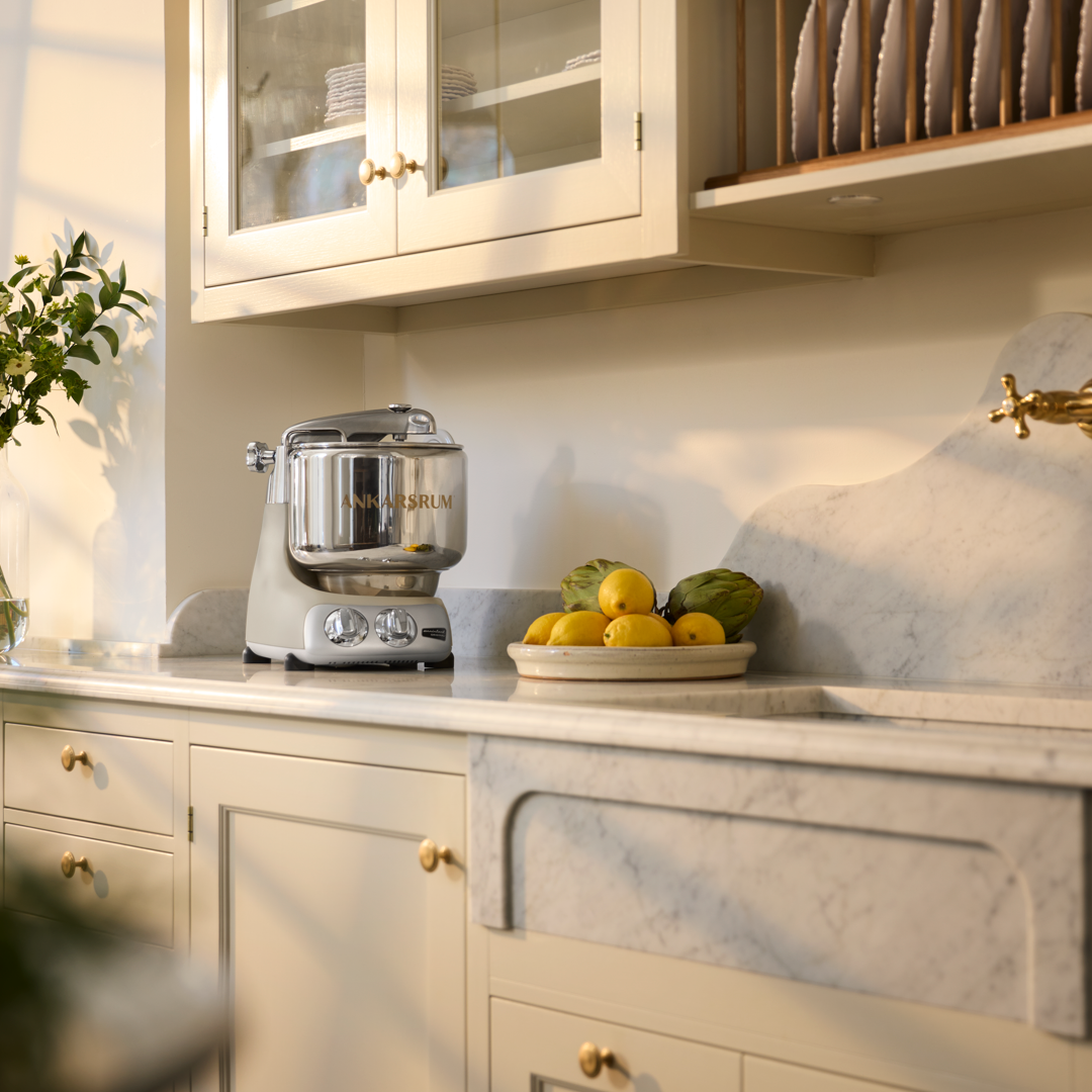 A kitchen with white cabinets and marble counter tops. A bowl of lemons and a Harmony beige stand mixer on it.