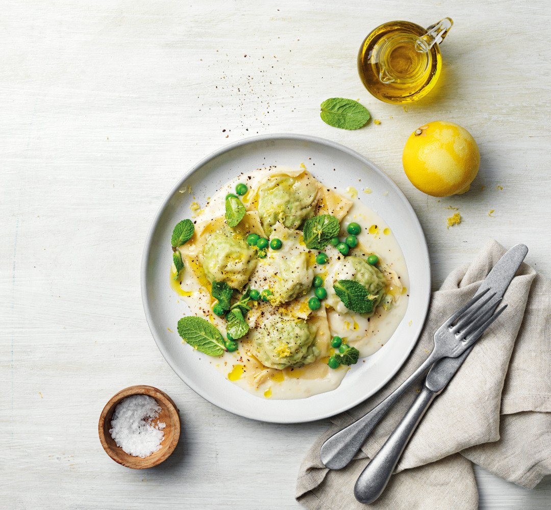 Ravioli med spenat och ricotta, toppad med ärtor. Bestick placerade bredvid, tillsammans med salt och en citron.