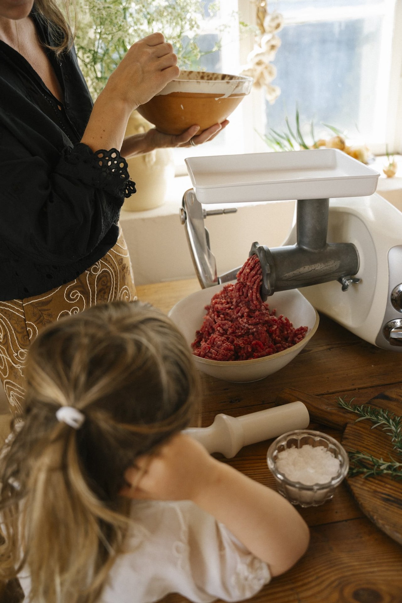 A woman and a little girl are grinding meat with an Ankarsrum assistent original.