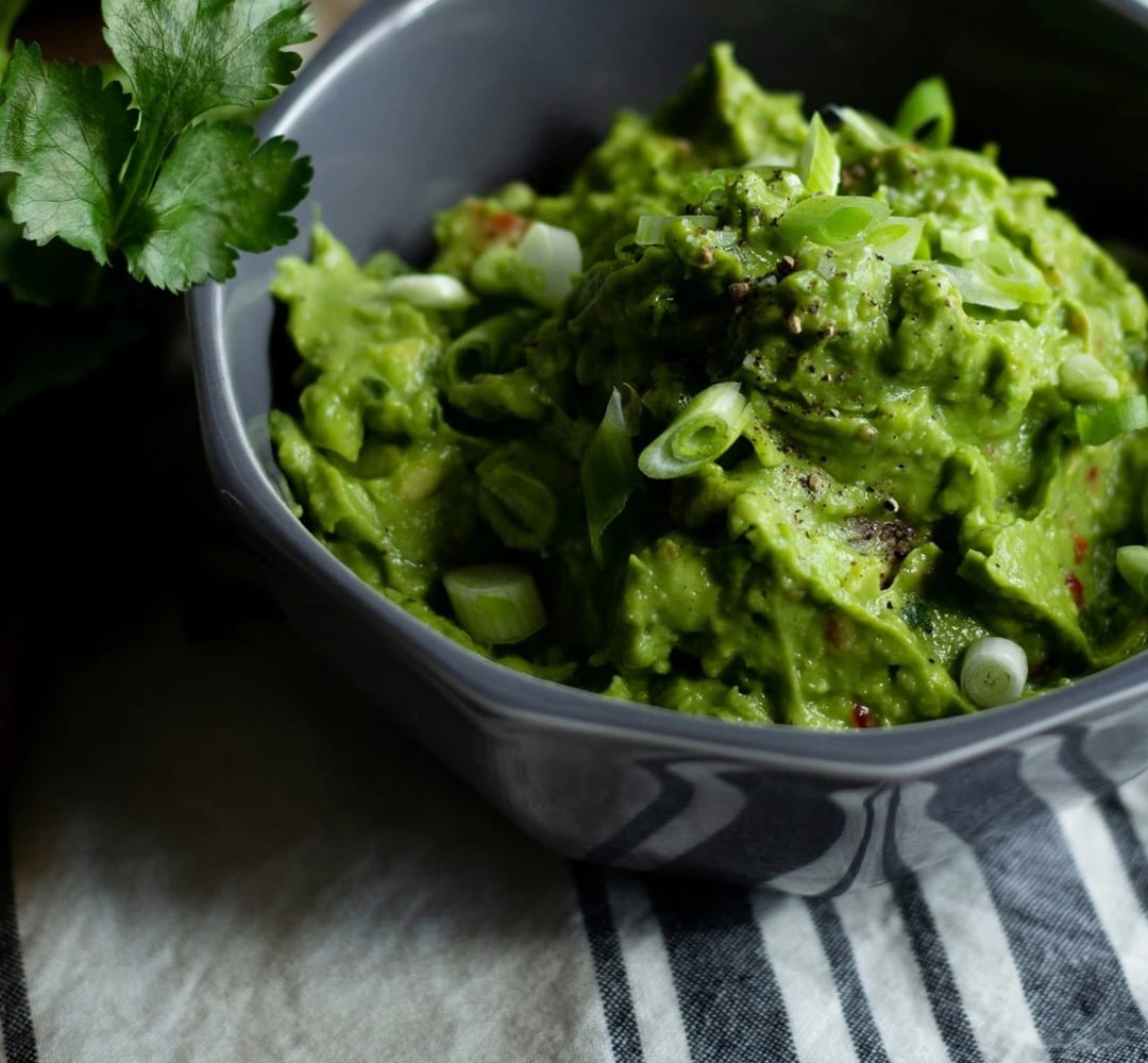A bowl of guacamole with a garnish on top.