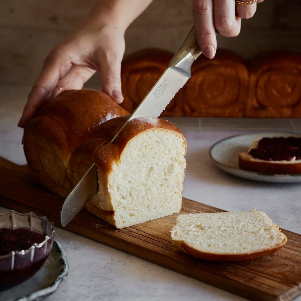 A person cutting a loaf of bread on a cutting board.