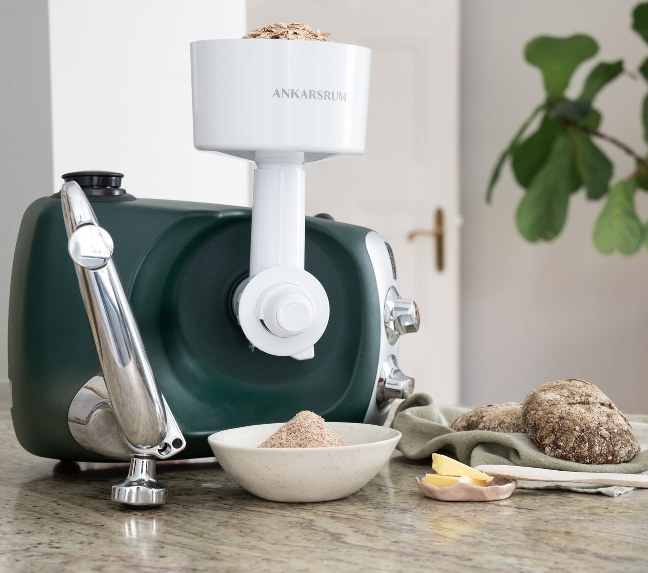 A grain mill attached to an Ankasrum stand mixer sitting on top of a counter.