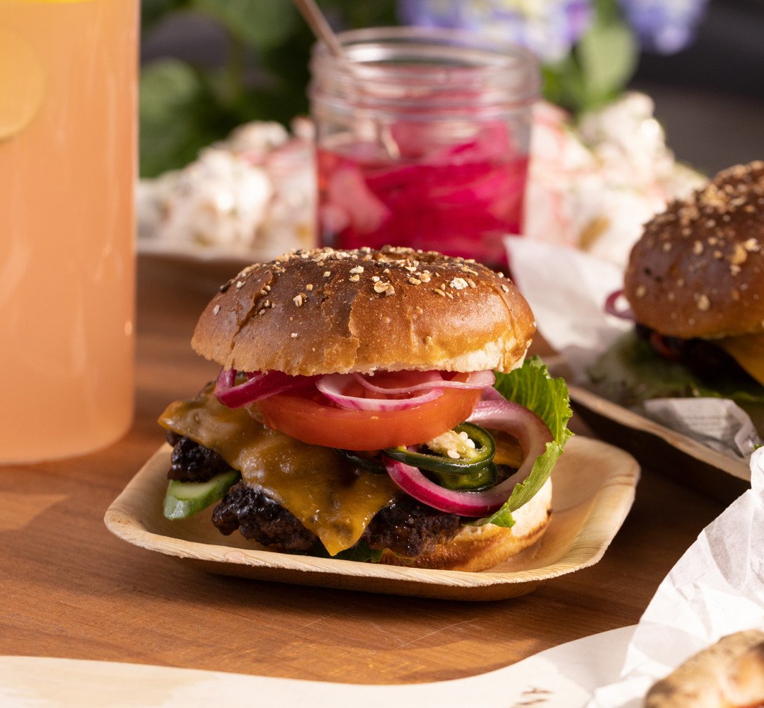 Smashed burgare i en hamburgerbröd med sallad, tomat och röd lök. På ett bord.