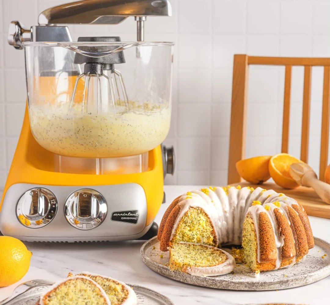 A freshly baked lemon cake on a kitchen table, with an Ankarsrum Assistant in the background.