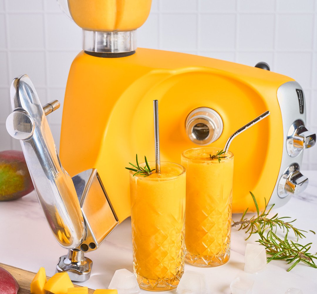 En mixer fylld med hemgjord mango frosé, med två glas vid sidan om.