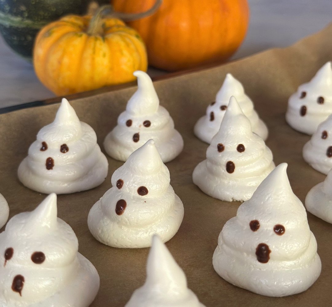 En Halloween-tårta toppad med marängspöken. En Ankarsrum Assistent bredvid tårtan med vispskålen, omgiven av fler marängspöken och pumpor.