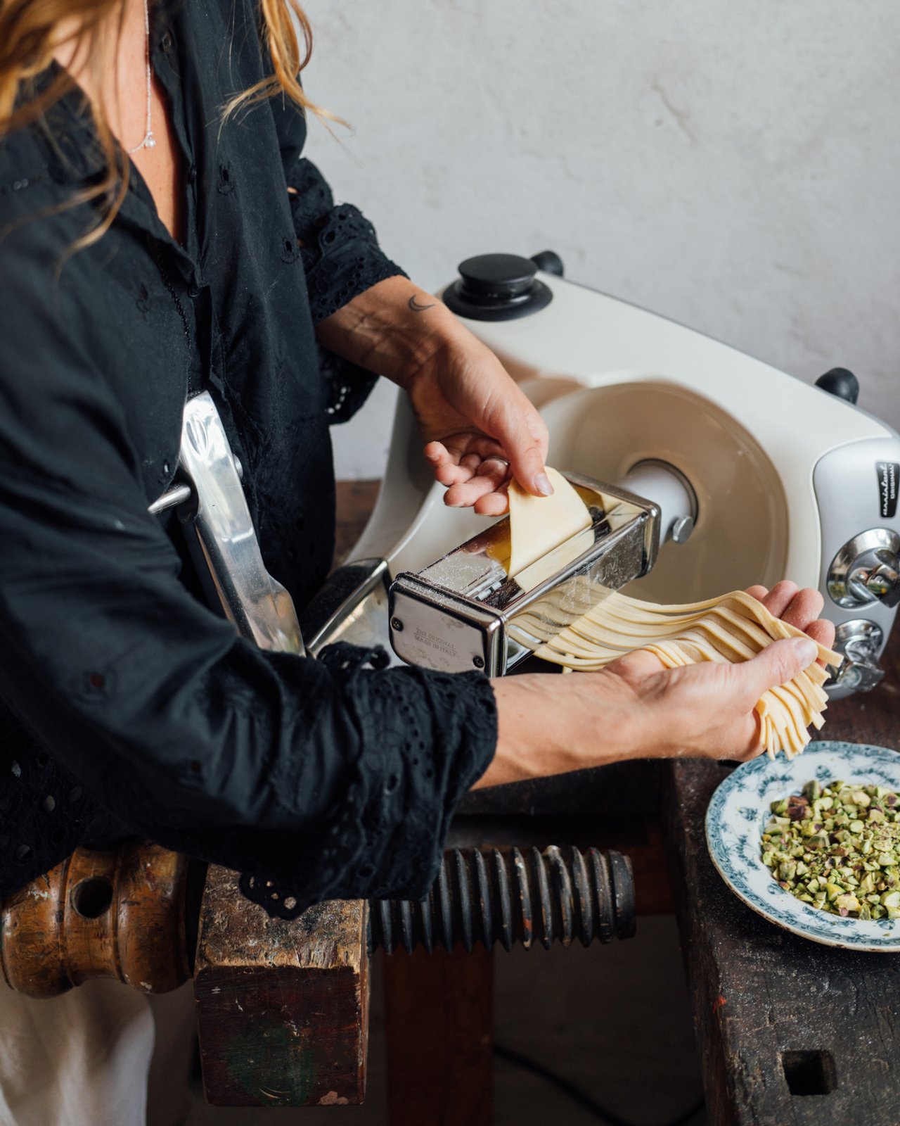 A woman is making pasta with an Ankarsrum Assisten original in a kitchen.