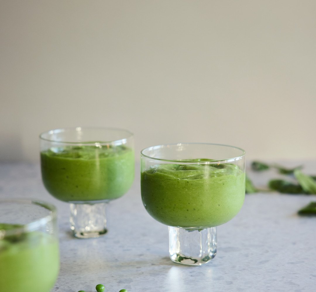 Green smoothie in three glasses on a light kitchen table.