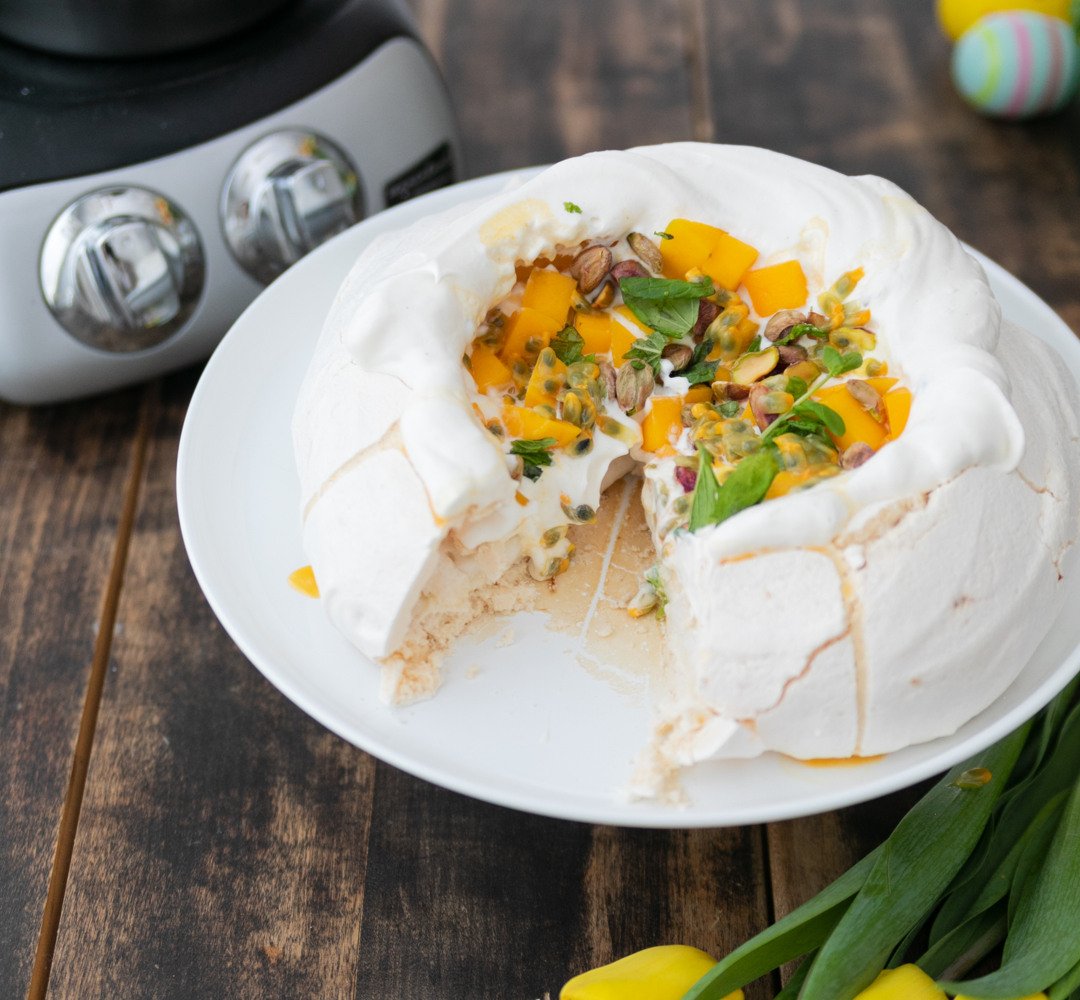 En vit tallrik med en pavlova bredvid gula blommor.