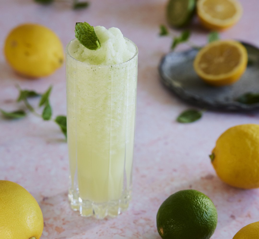 Ett glas lemonad med mynta som dekoration och citroner runtomkring.