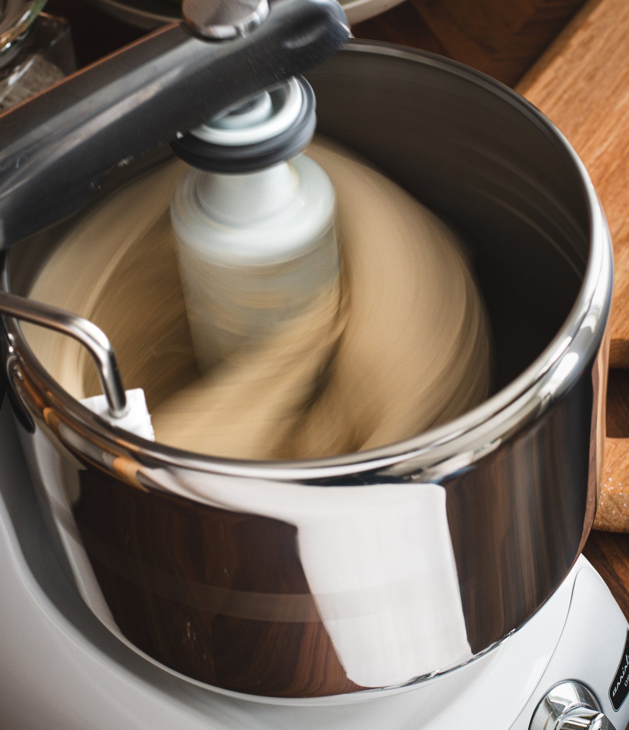A large metal bowl with a doughroller and doughknife mixing a dough.