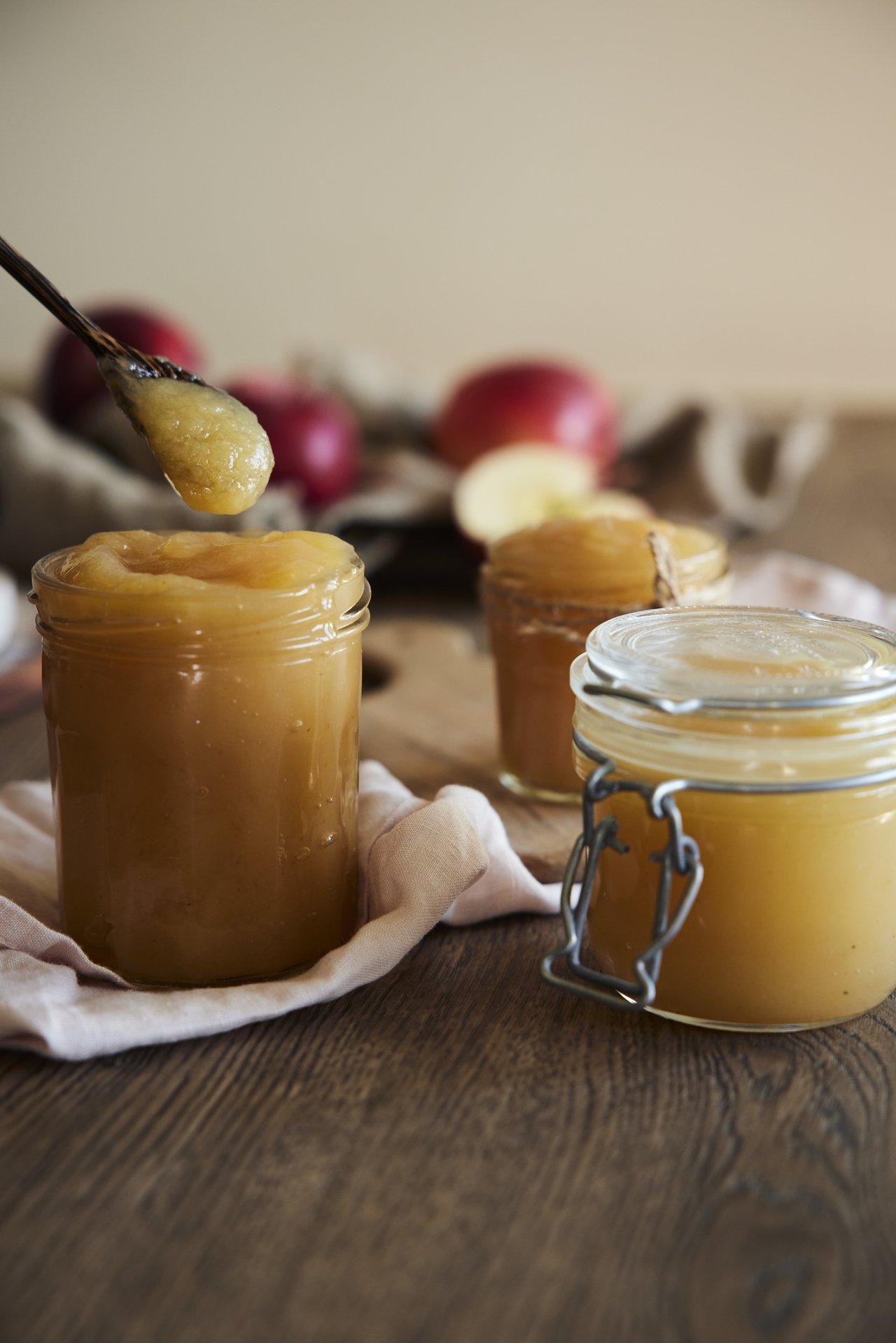 Two jars of apple jam on a table with apples in the background.