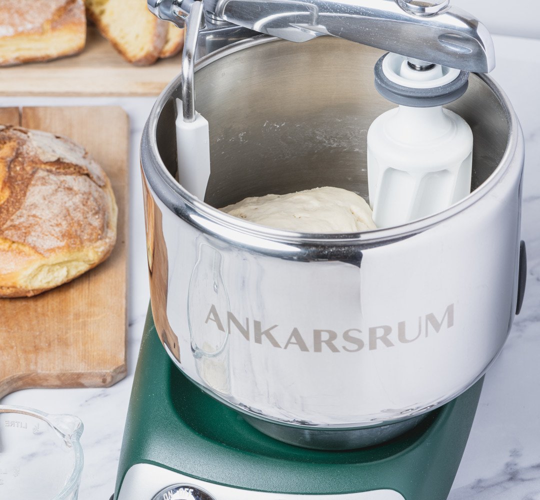 Ankarsrum assistent i skogsgrön, stående på en bänk. Bakar bröd.