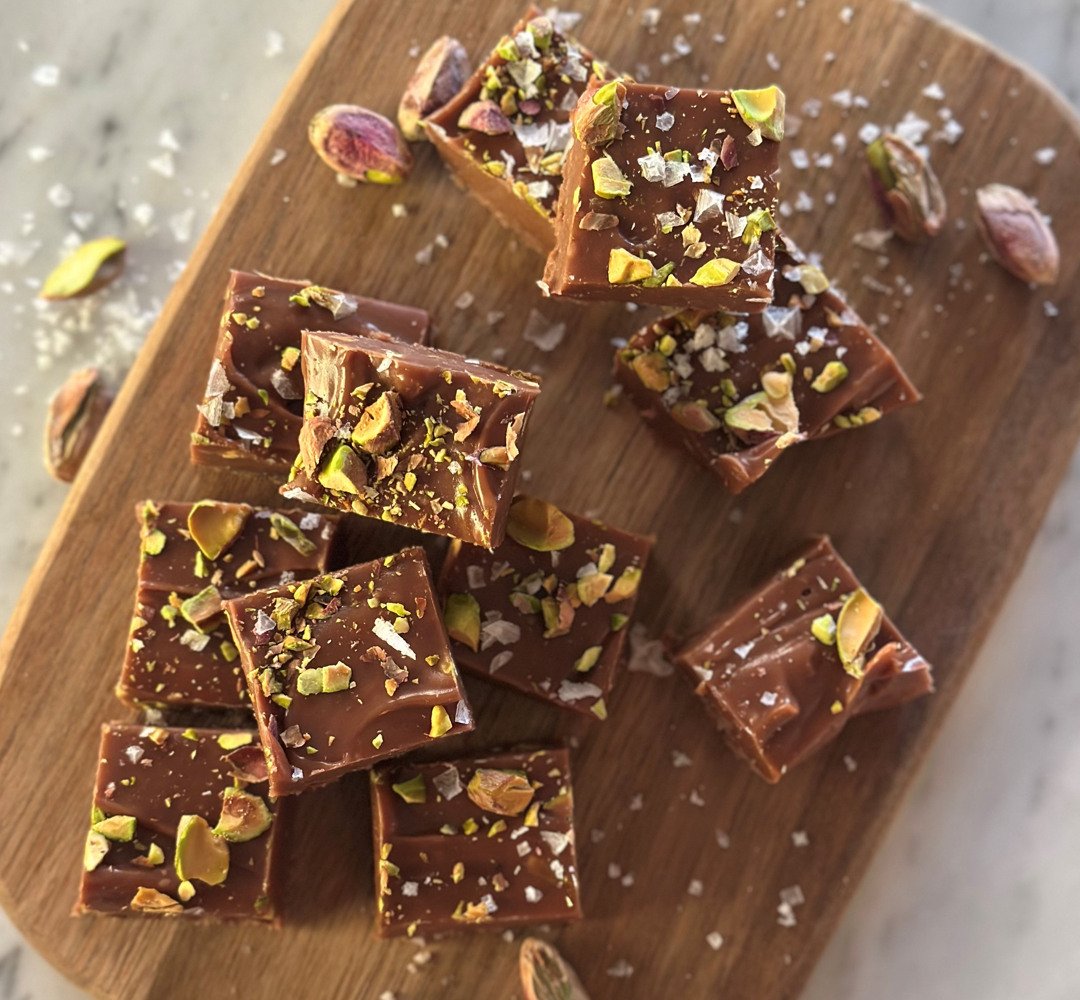 En skärbräda i trä med bitar av chokladfudge och pistagenötter.