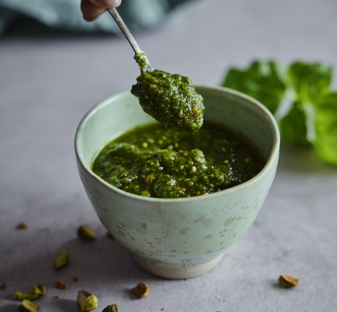 En person doppar pesto i en liten skål.
