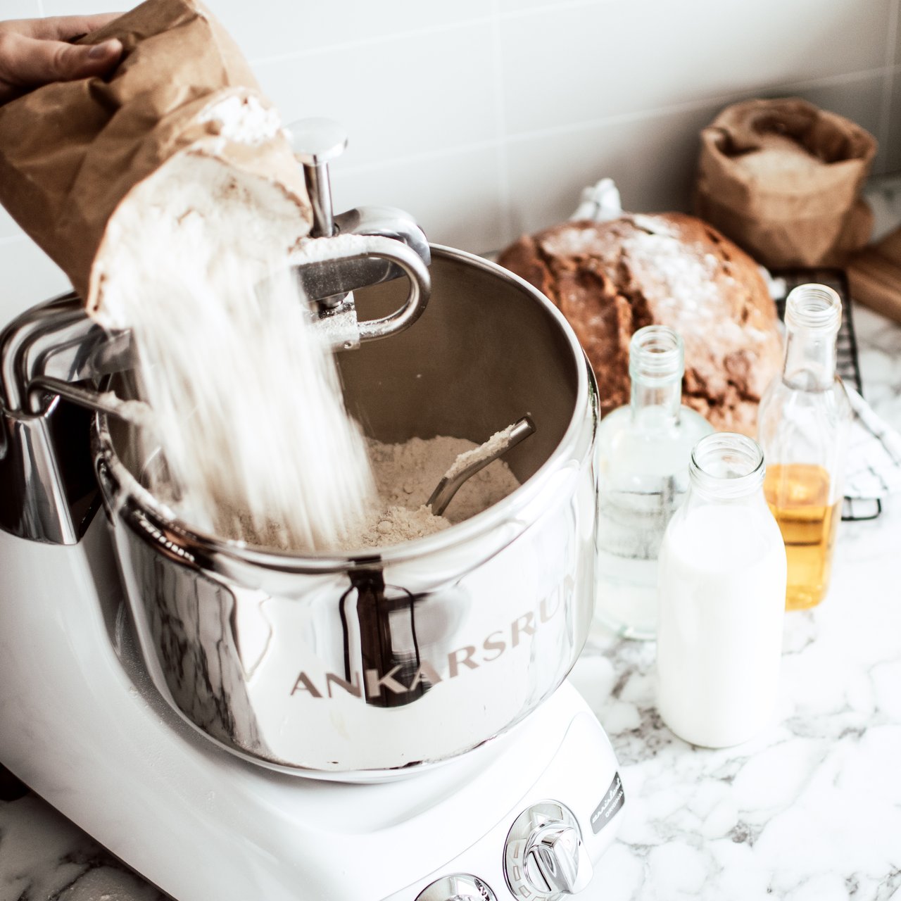 A person is pouring flour into a steel bowl where the dough hook is attached.