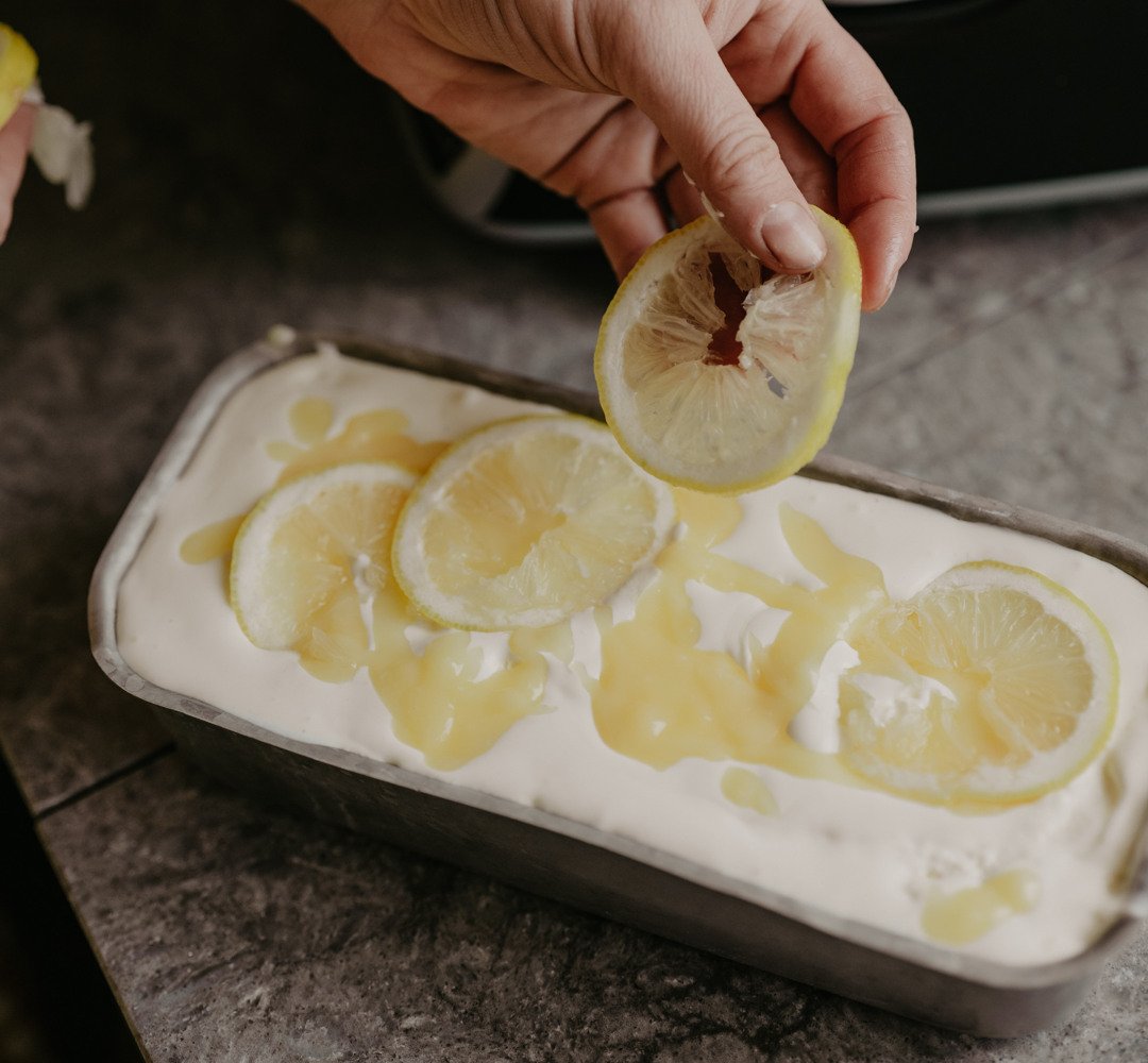 A person is squeezing a lemon into bowl of ice cream