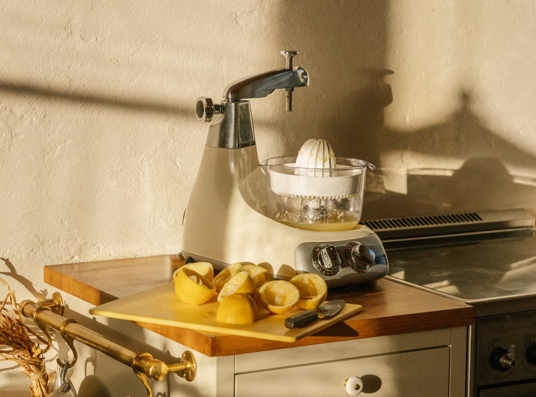 A kitchen counter with a lemons and a creme light stand mixer with a citrus press accessory.