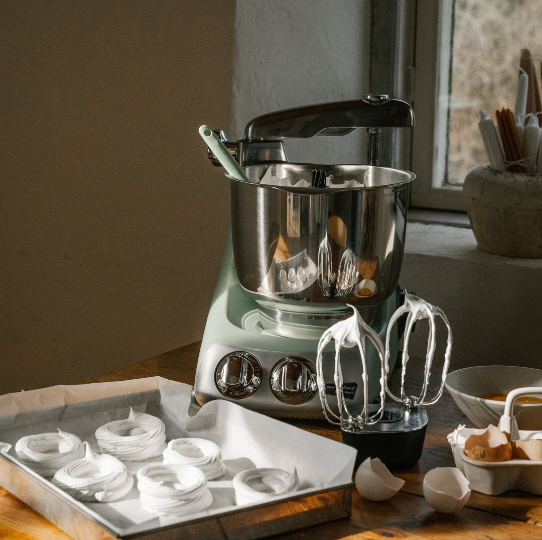 En kvinna dekorerar cupcakes med en spritspåse. På bordet står en Ankarsrum Assistent Original i Cloudy Pink, monterad med en vispskål i rostfritt stål.