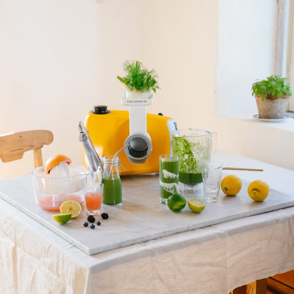 Ett bord med en Ankarsrum Assistans Original i Sunbeam Yellow, mixern, citruspressen, citroner, limefrukter och juice.