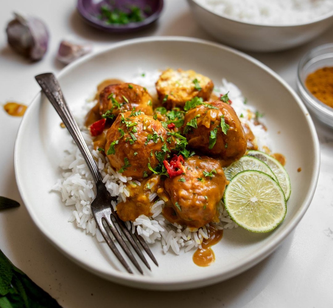En vit tallrik med ris och köttbullar i en krämig sås.