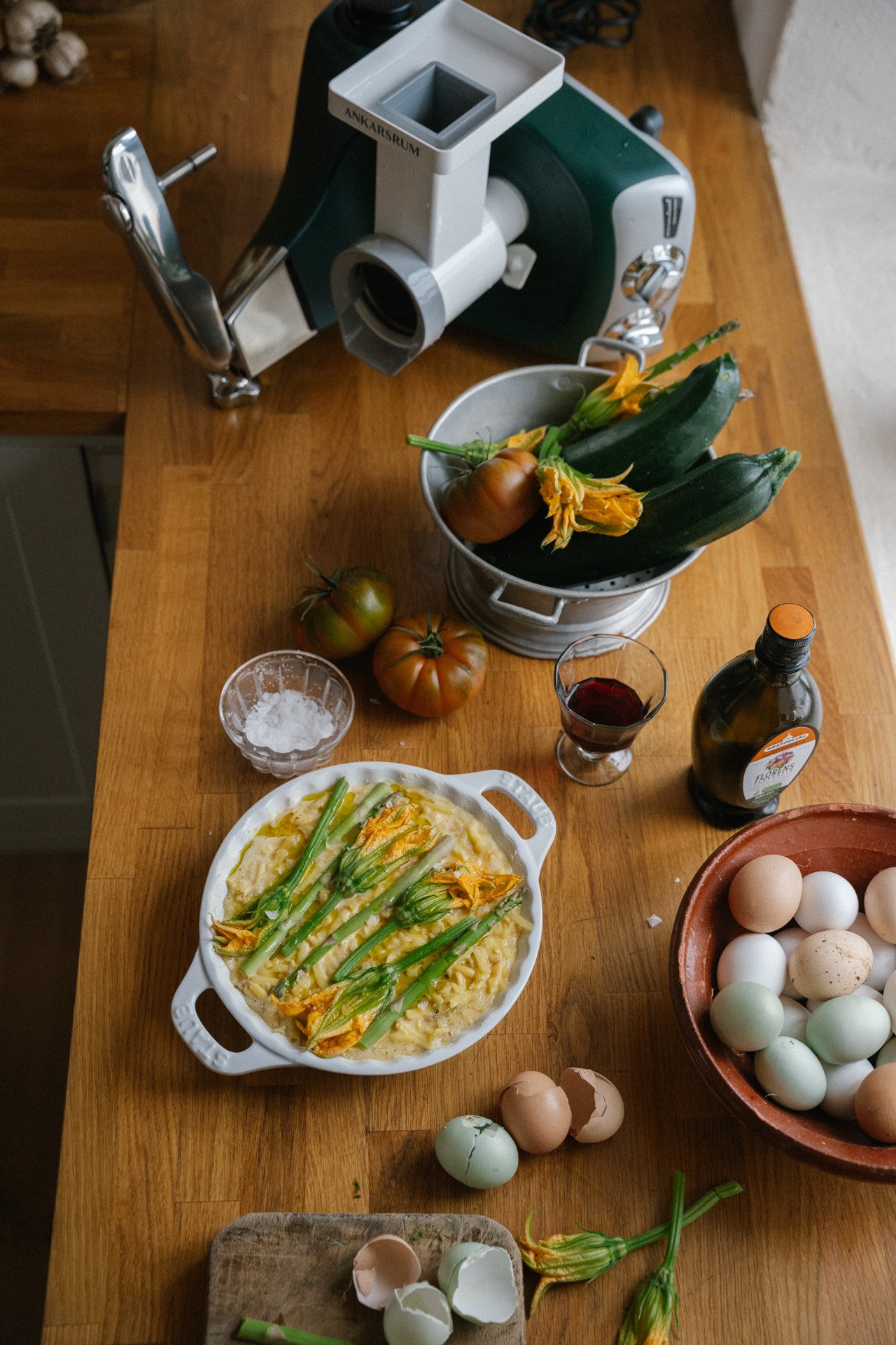 A wooden table topped with bowls of food and an Ankarsrum assistent original with a vegetable cutter attached.