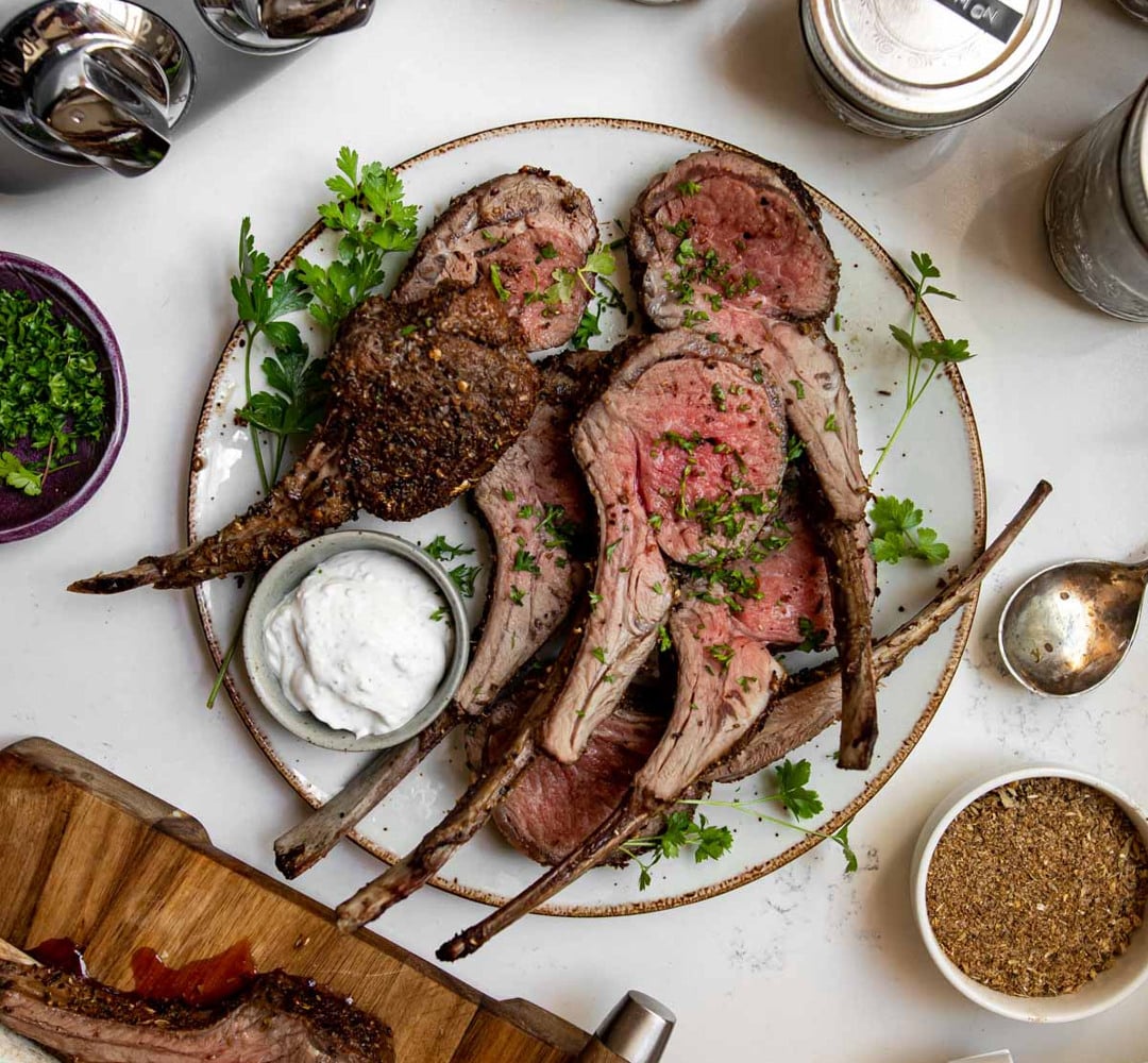 A chai-crusted rack of lamb with yogurt sauce on a plate.