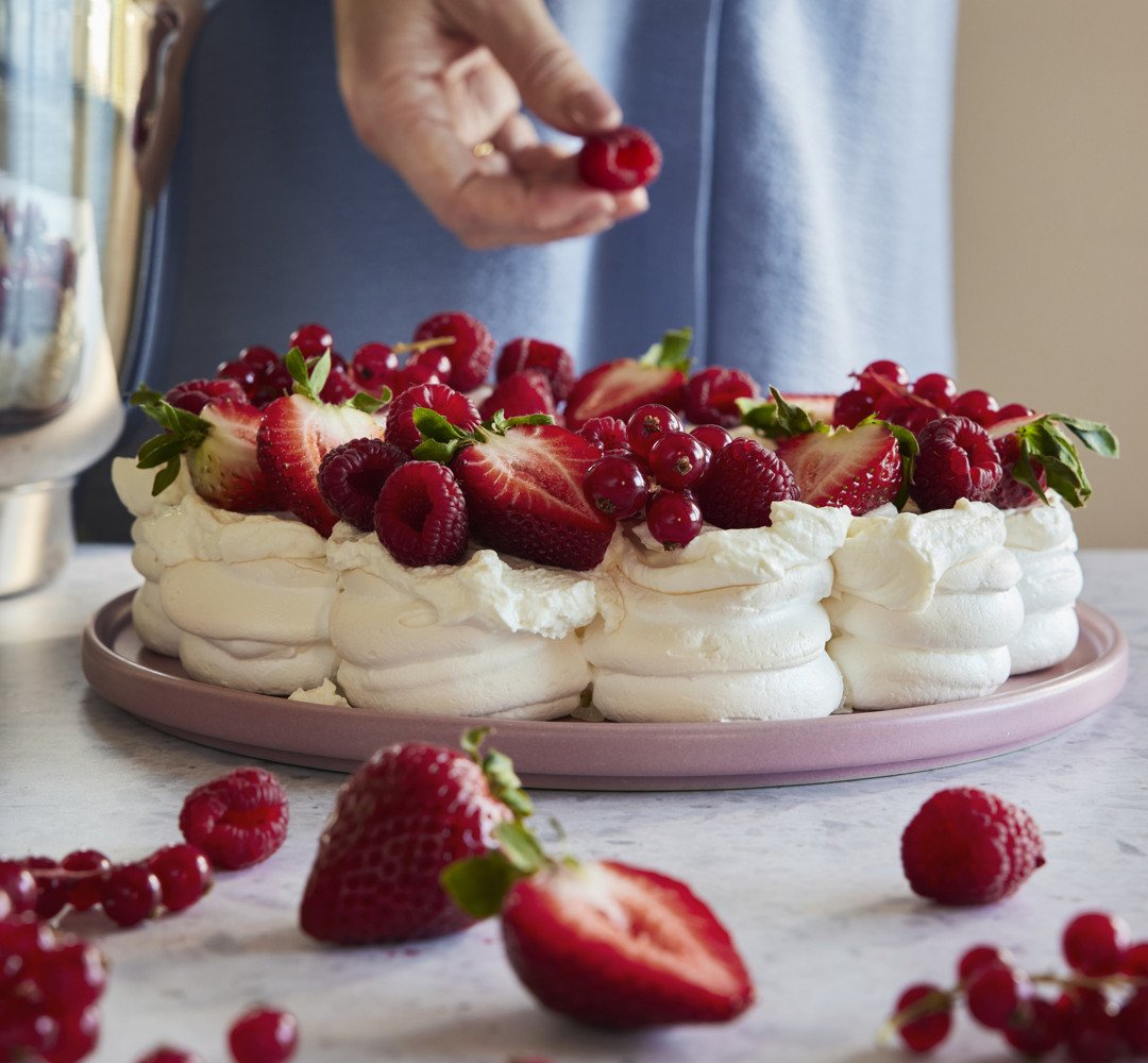 Pavlova on a table with a person adding raspberries.
