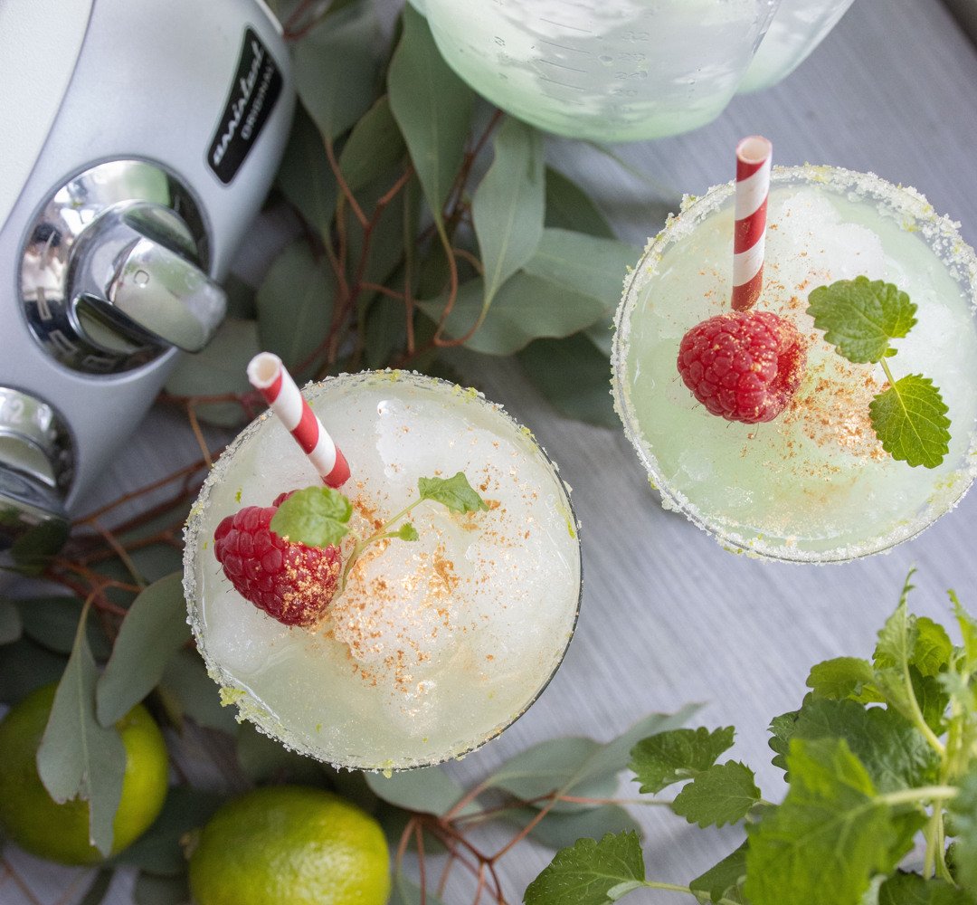 Two margaritas with strawberries and garnish on a table.