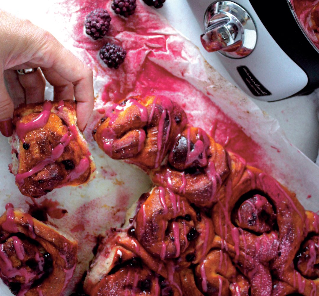 A person holding a piece of buns with raspberries on it.
