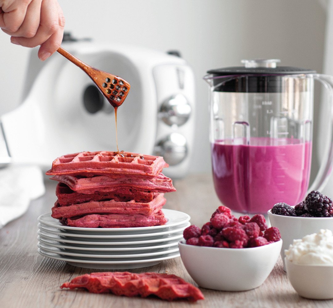 En person som häller något över en tallrik med rosa våfflor.