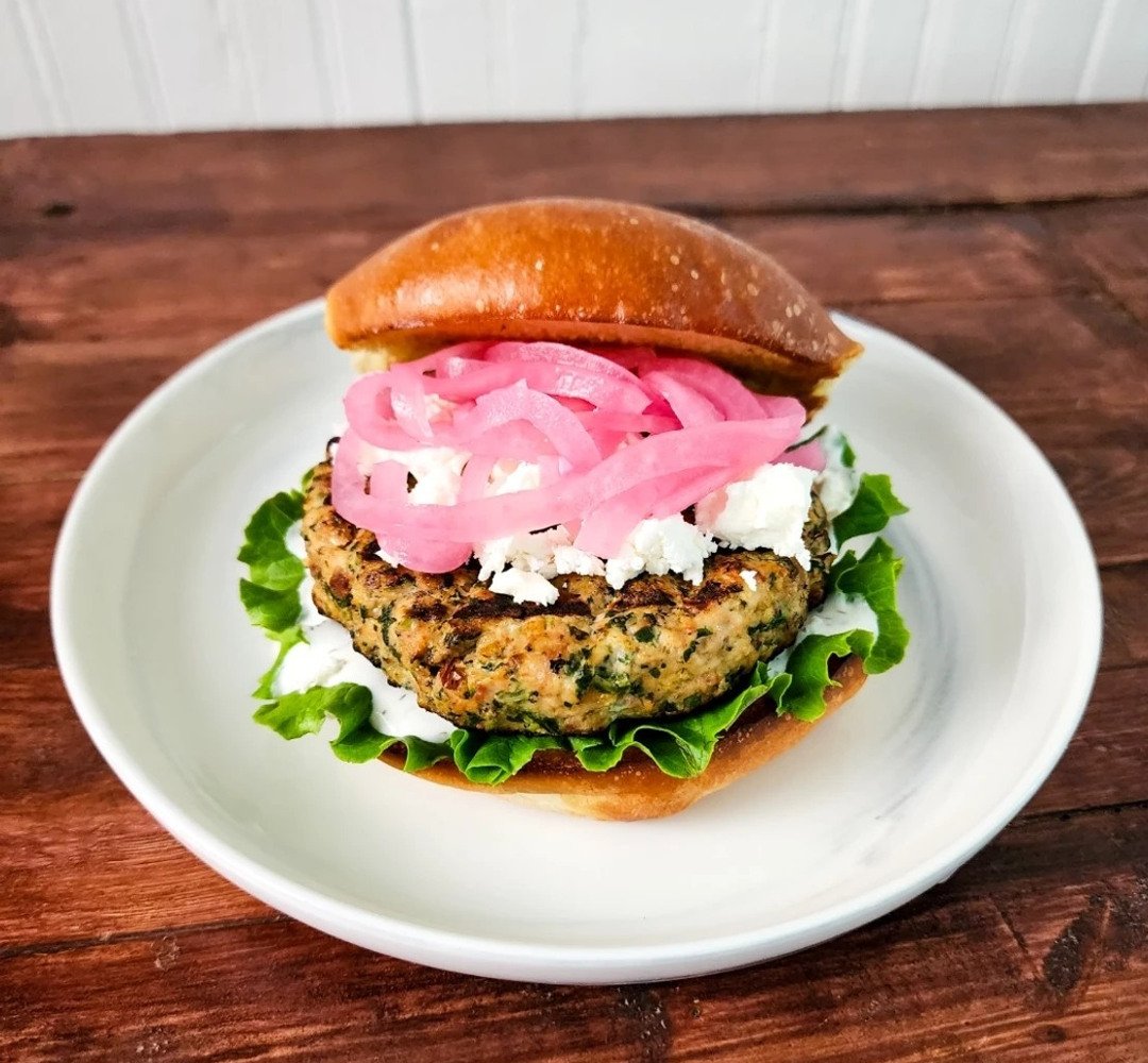 En hamburgare med lök och sallad på en vit tallrik.
