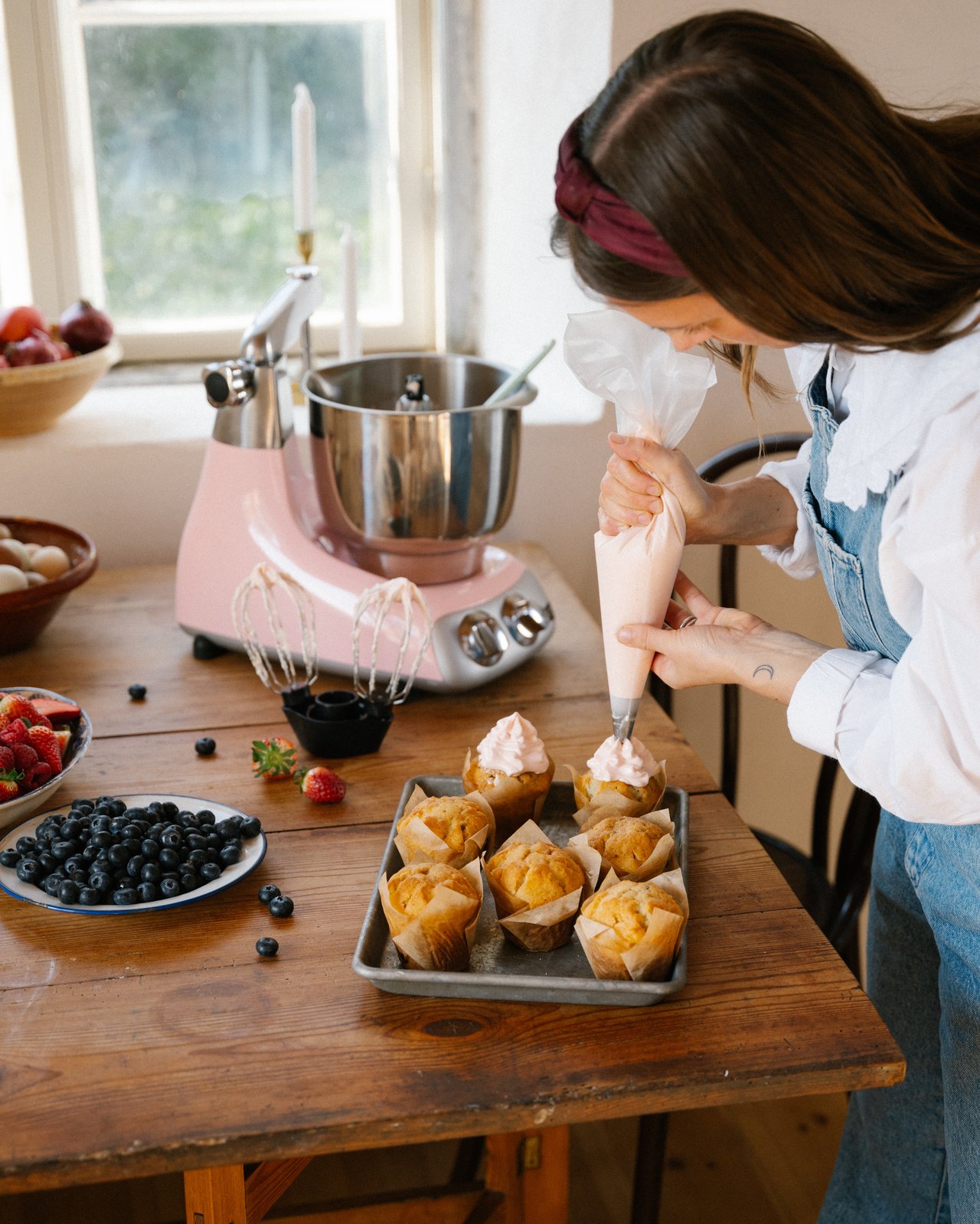 A woman standing in front of a table and decorating cupcakes.
