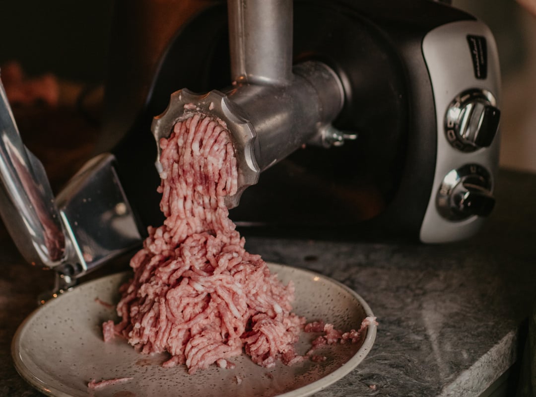 En person som använder en köttkvarn för att göra köttfärs.