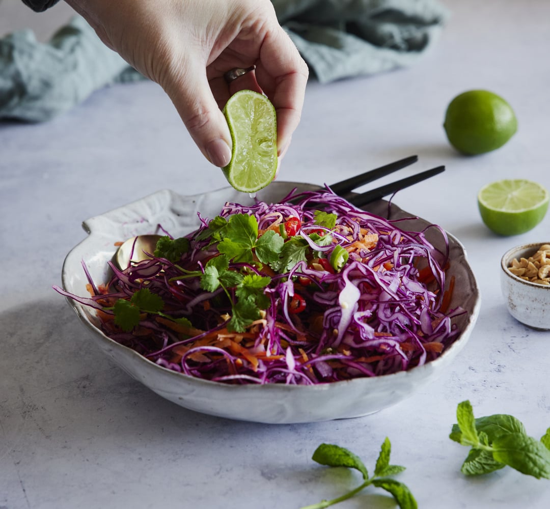 En person doppar en lime i en skål med coleslaw.