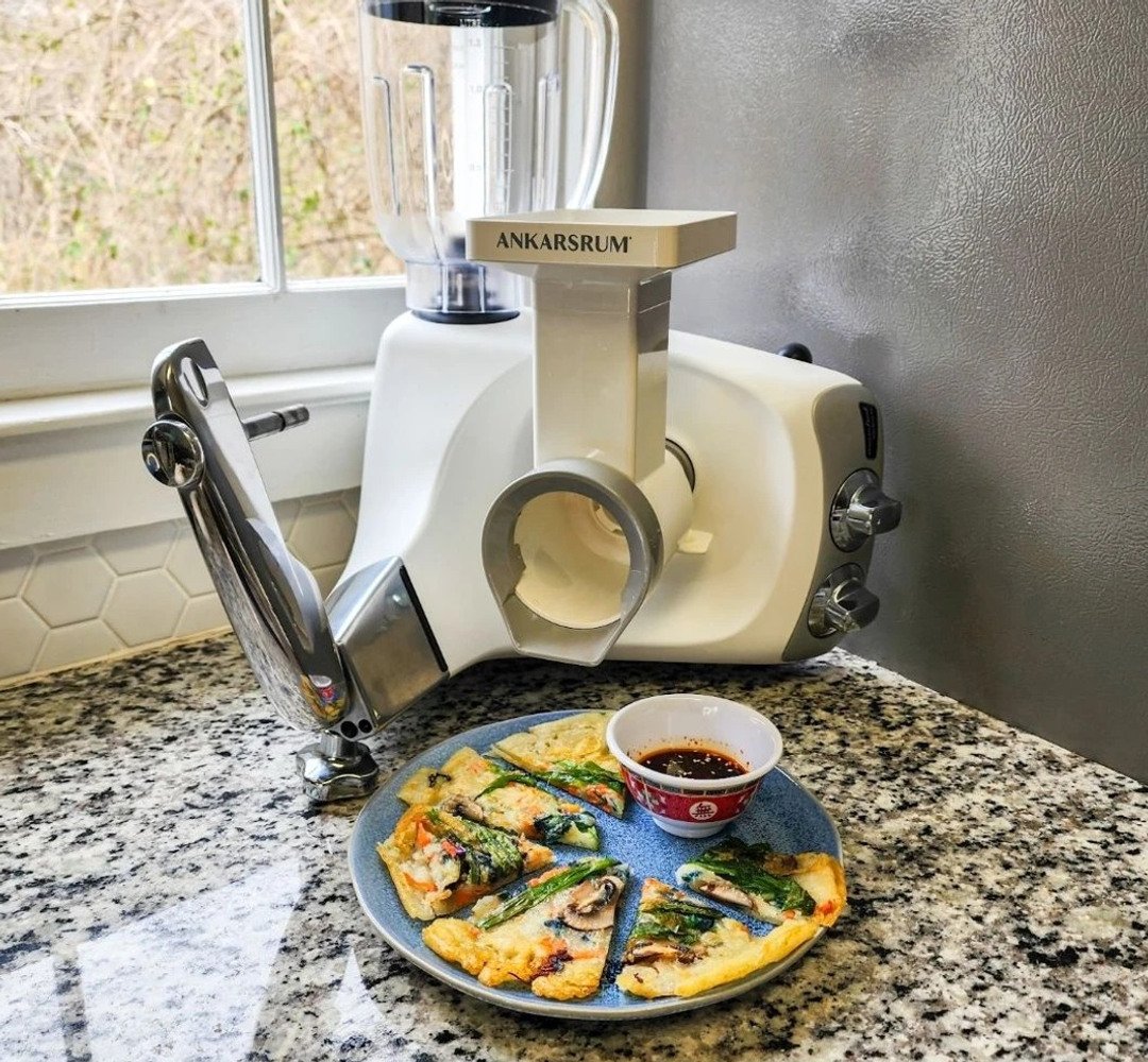 Ankarsrum Assistent med mixer och grönsakskärare fästa. En tallrik med crêpes står framför.