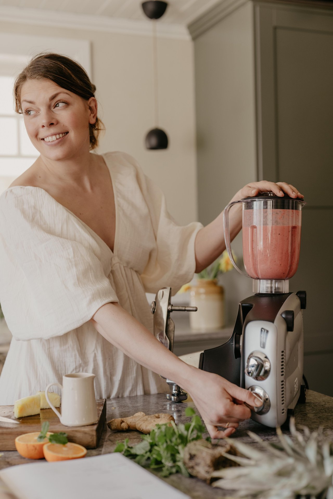 En kvinna använder Blender-tillbehöret på en Ankarsrum Assistent Original i Harmony Beige för att förbereda en rosa fruktsmoothie i ett ljust kök.