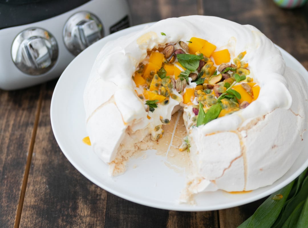 En vit tallrik med en pavlova bredvid gula blommor.