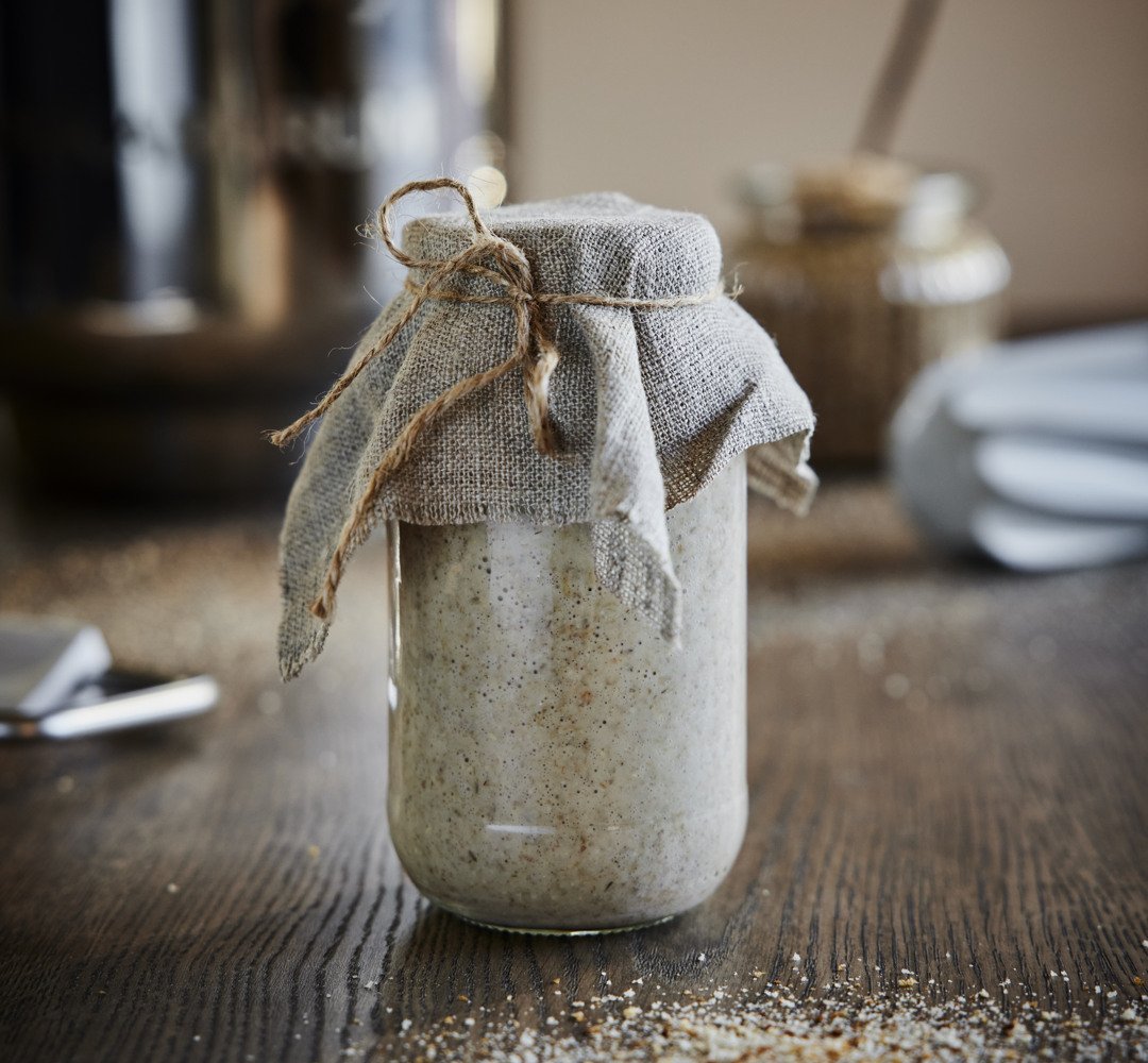 A glass jar containing sourdough starter, with a cloth wrapped around the jar.