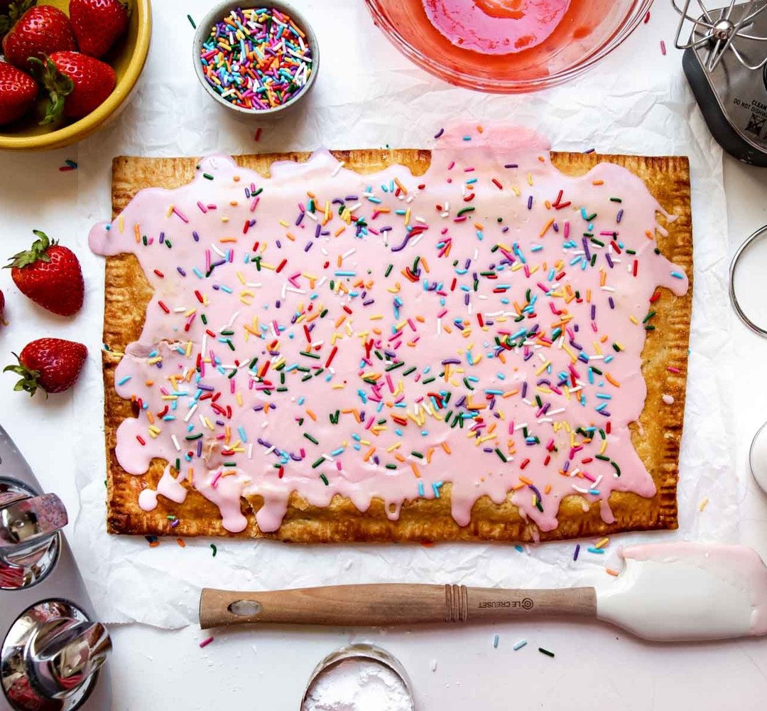 A strawberry pastry tart with pink frosting and sprinkles on it.