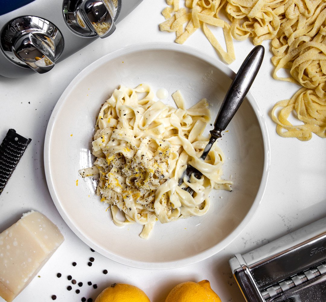 A plate of pasta with cheese and lemons next to a toaster.