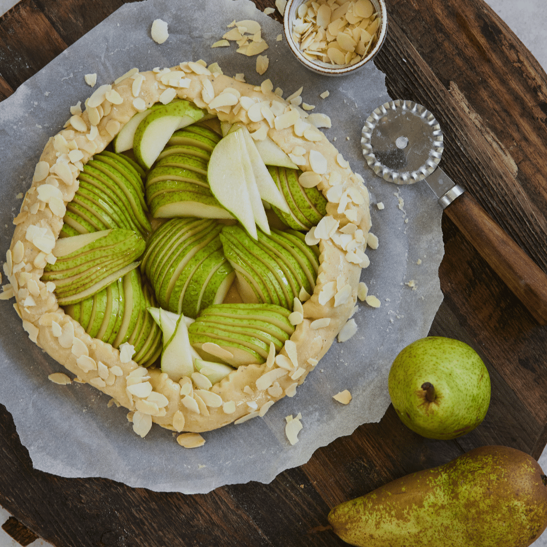 Päärynägalette, jossa on viipaloituja vihreitä päärynöitä ja mantelilastuja rustiikkisella puupöydällä.