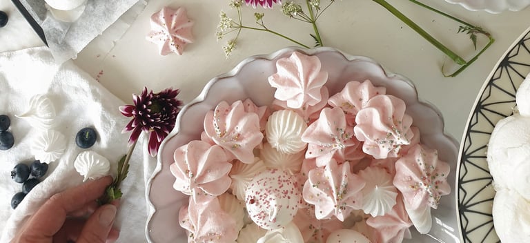 Ett bord täckt med tallrikar av maräng och blommor.