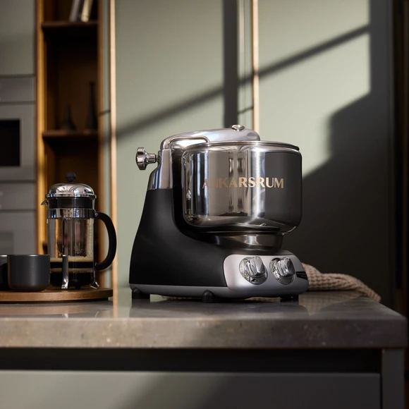 Ankarsrum Assistent Original en noir sur un plan de travail de cuisine en marbre, avec une cafetière à piston noire à côté.