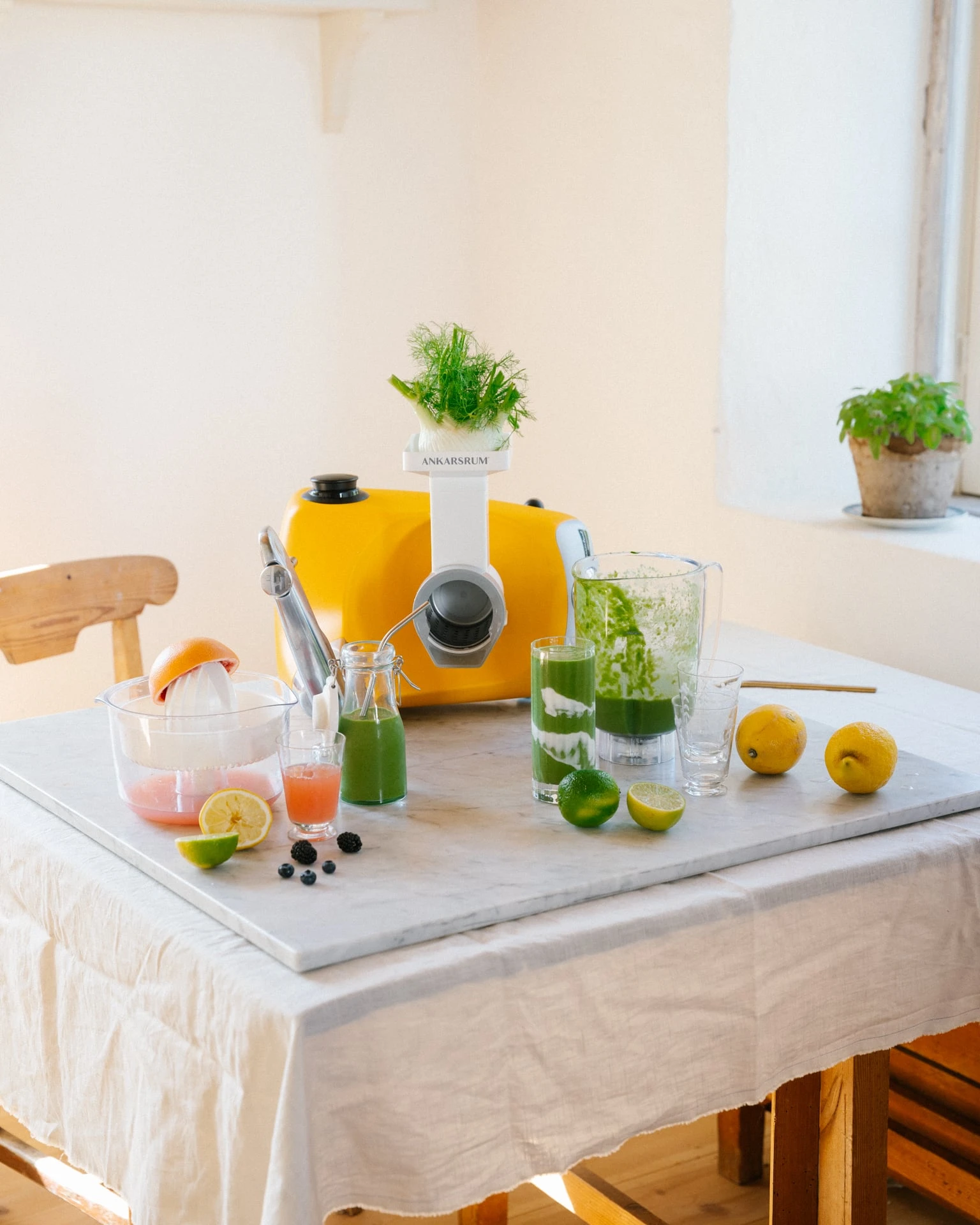 Gul Ankarsrum Assistent med juicepress, gröna juicer, lime, citroner och färsk dill på ett marmorbord.